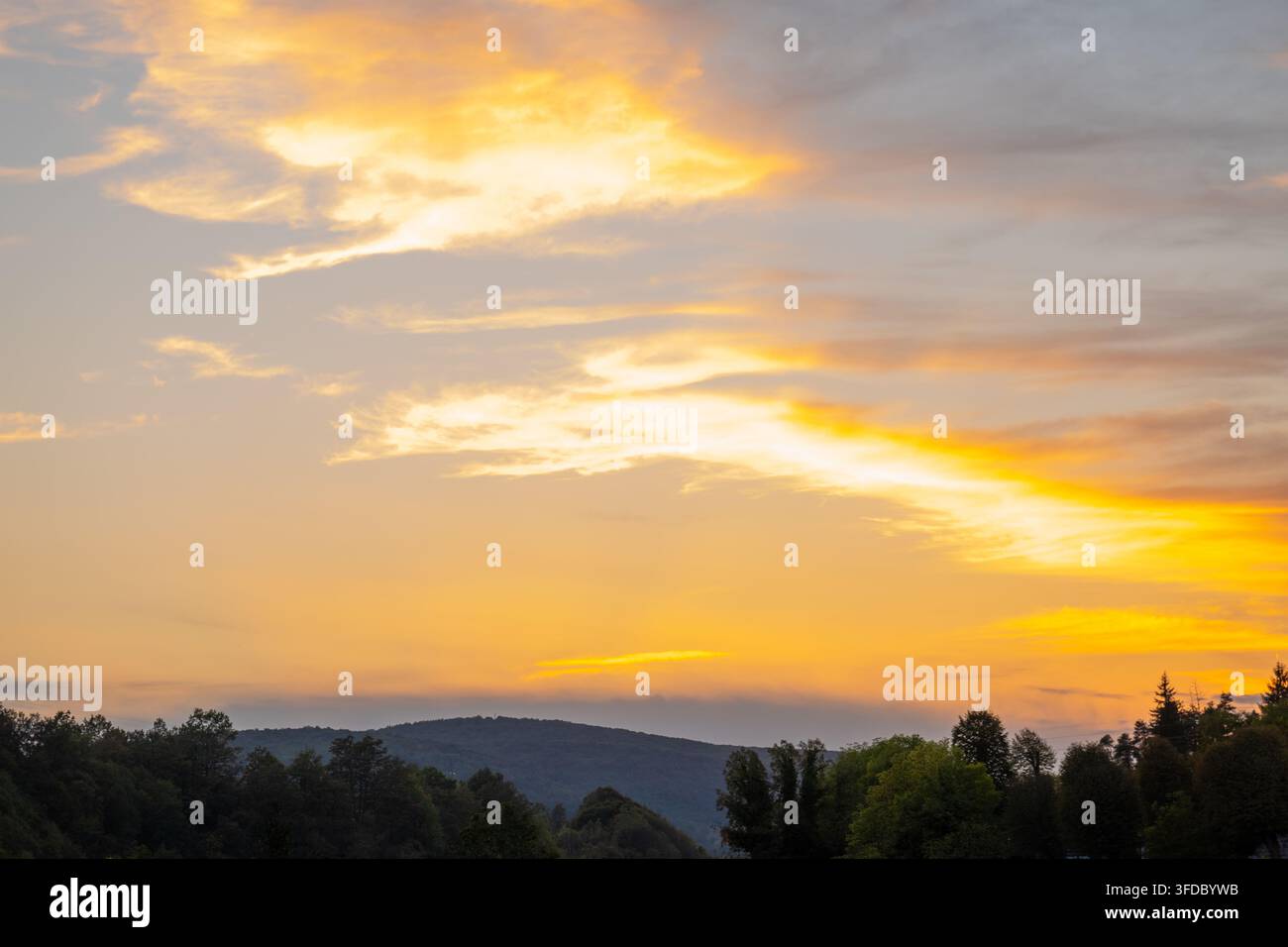 Nuvole dorate del tramonto su colline boschive e un tranquillo paesaggio serale Foto Stock