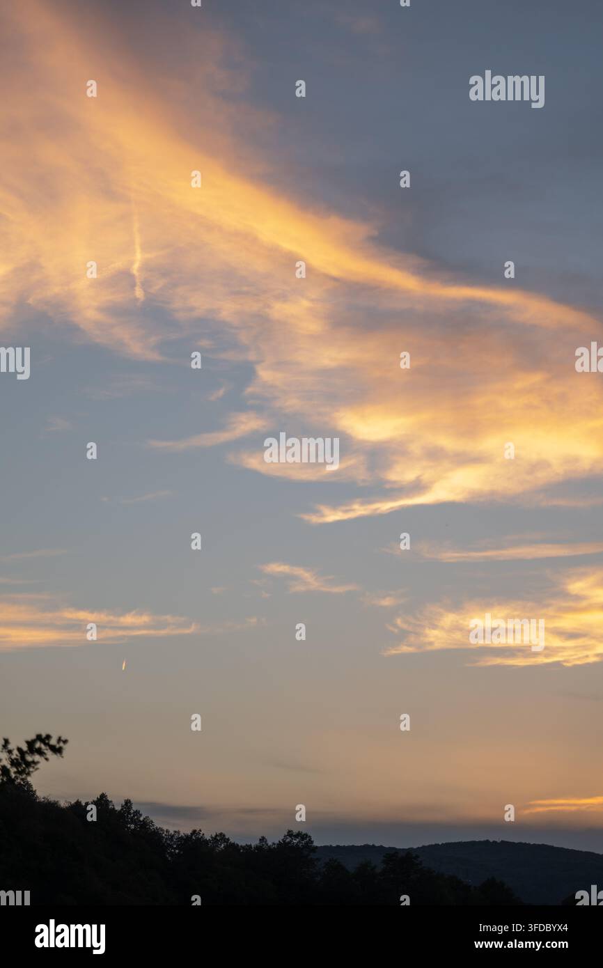 Nuvole dorate del tramonto che brillano sopra colline scure e un orizzonte boschivo in silhouette Foto Stock