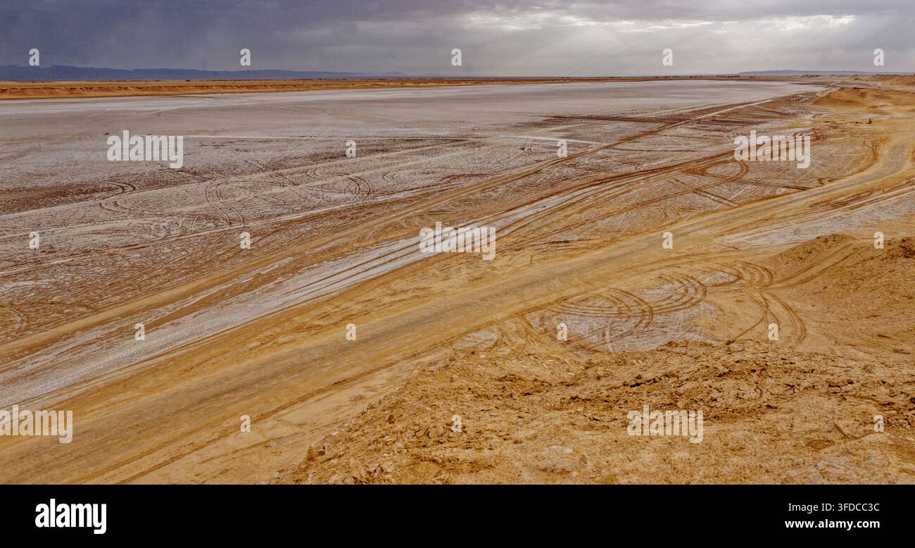 Veduta ampia sulla pianura salina di Chott el Djerid segnata dalle tracce degli pneumatici dei veicoli fuoristrada sotto un cielo tempestoso drammatico a Ong Jmal, Tunisia. Cattura Foto Stock