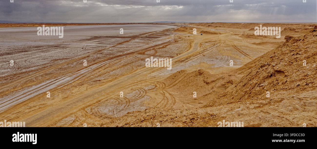 Veduta ampia sulla pianura salina di Chott el Djerid segnata dalle tracce degli pneumatici dei veicoli fuoristrada sotto un cielo tempestoso drammatico a Ong Jmal, Tunisia. Cattura Foto Stock