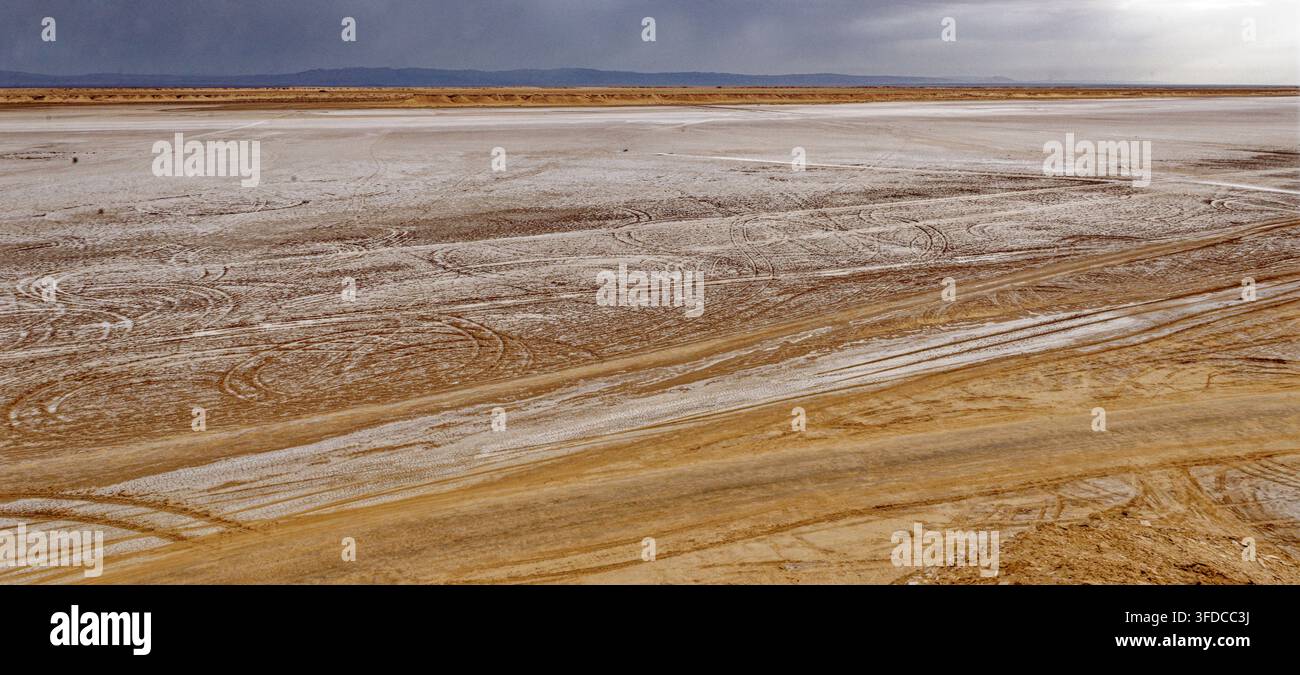 Veduta ampia sulla pianura salina di Chott el Djerid segnata dalle tracce degli pneumatici dei veicoli fuoristrada sotto un cielo tempestoso drammatico a Ong Jmal, Tunisia. Cattura Foto Stock
