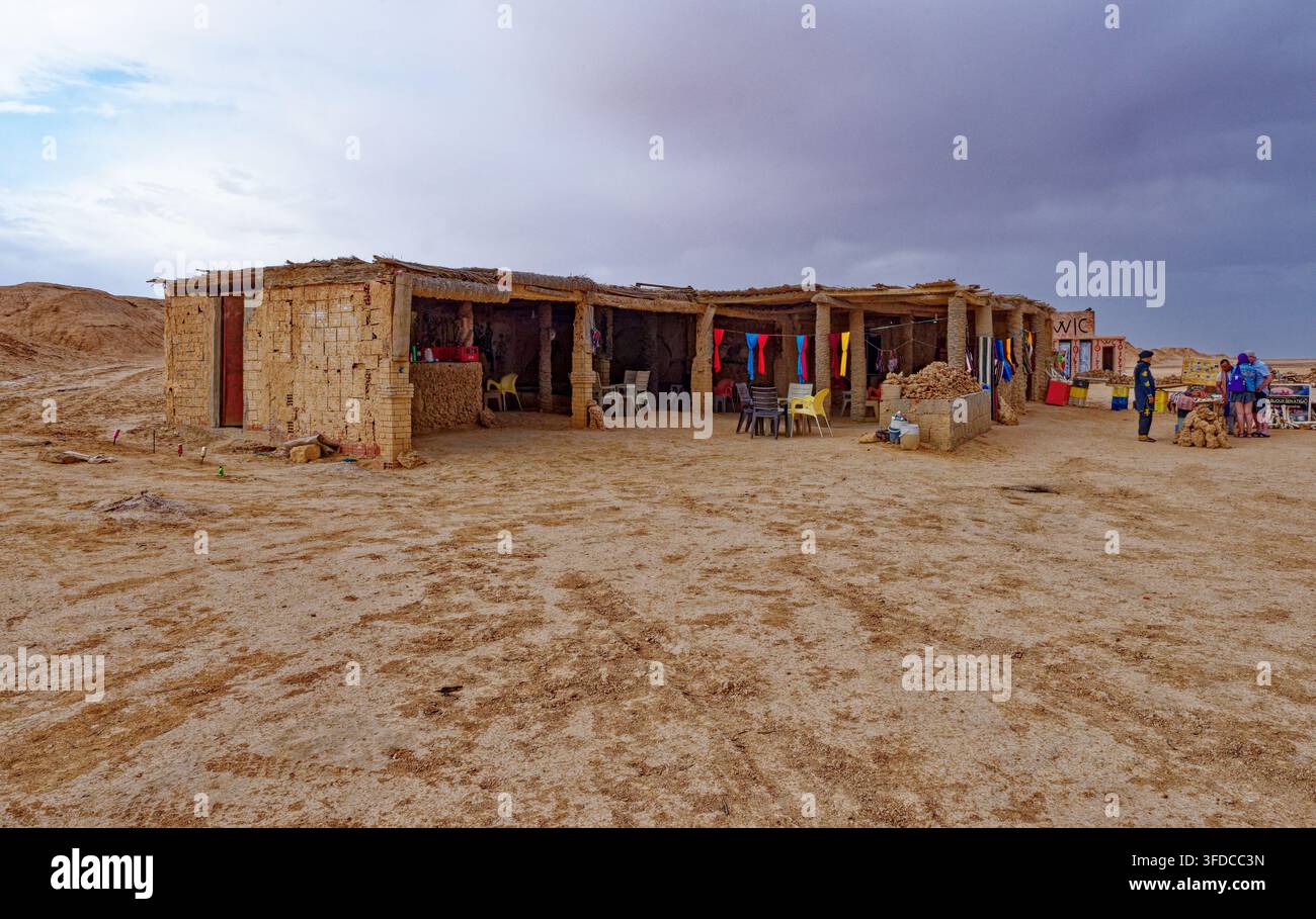 Edificio tradizionale in mattoni di fango che funge da caffè stradale e bancarella di souvenir sotto un cielo nuvoloso nel deserto di Ong Jmal, Tunisia. Fotografato il Foto Stock