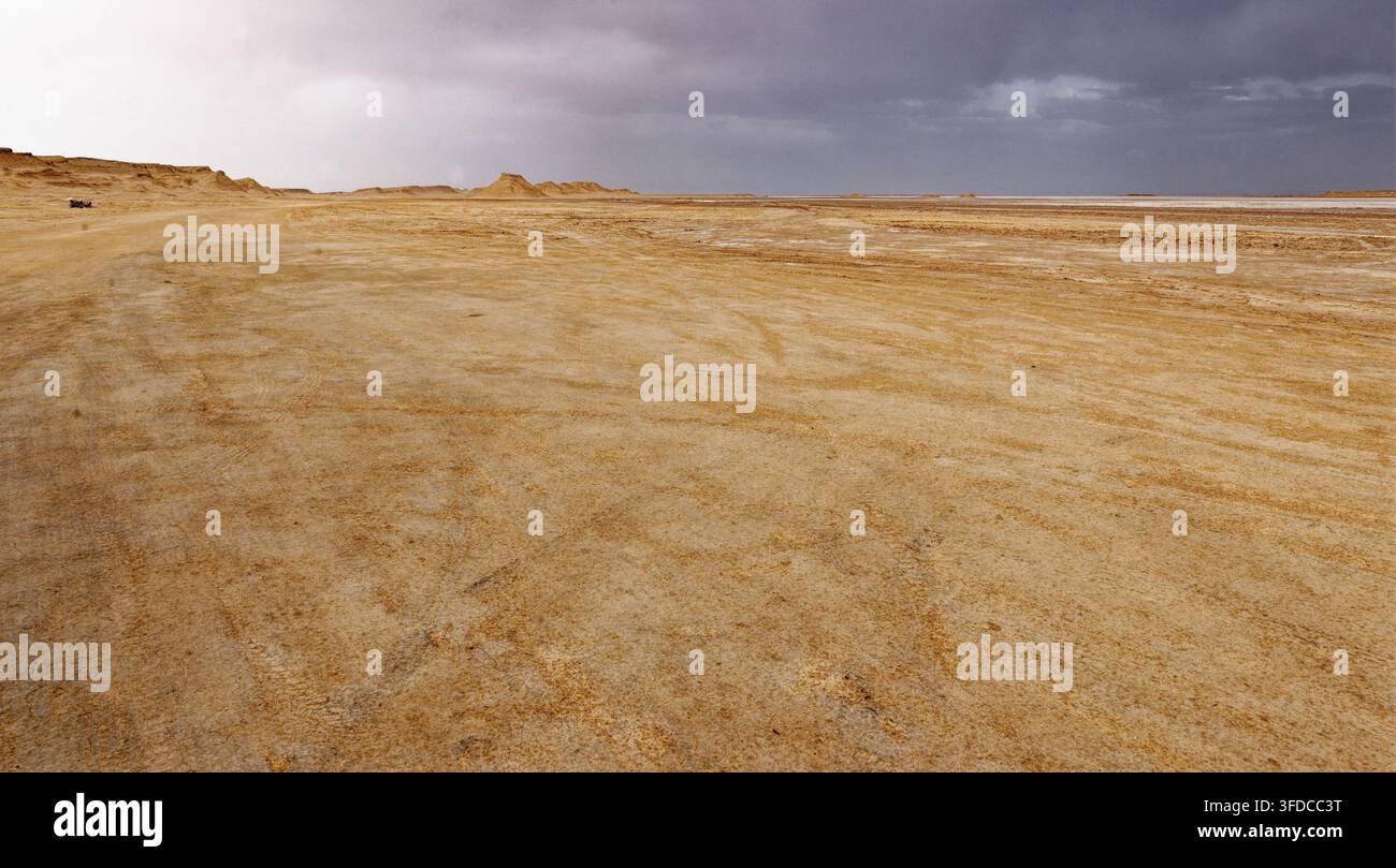 Ampia vista panoramica delle pianure desertiche estese attraversate da tracce di pneumatici fuoristrada che si estendono verso le distanti pianure salate a Ong Jmal, Tunisia. Scatto Foto Stock