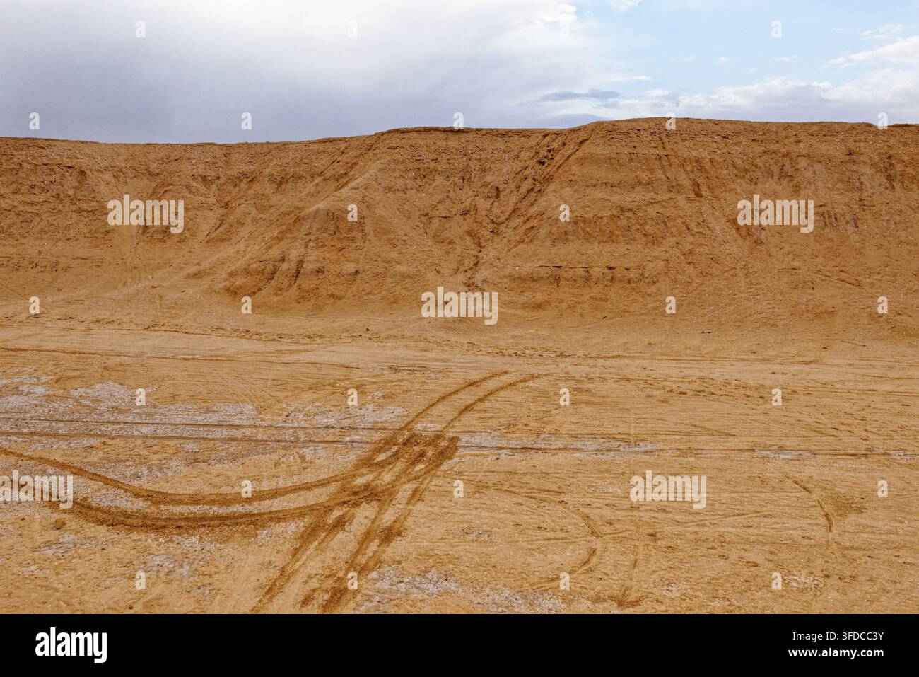Fondo di canyon desertico arido segnato da tracce di pneumatici che portano alle pianure salate sotto le scogliere di arenaria sotto un cielo nuvoloso a Ong Jmal, Tunisia. Catturato l'08 Foto Stock