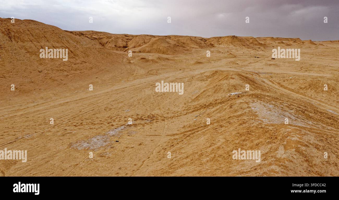 Fondo di canyon desertico arido segnato da tracce di pneumatici che portano alle pianure salate sotto le scogliere di arenaria sotto un cielo nuvoloso a Ong Jmal, Tunisia. Catturato l'08 Foto Stock