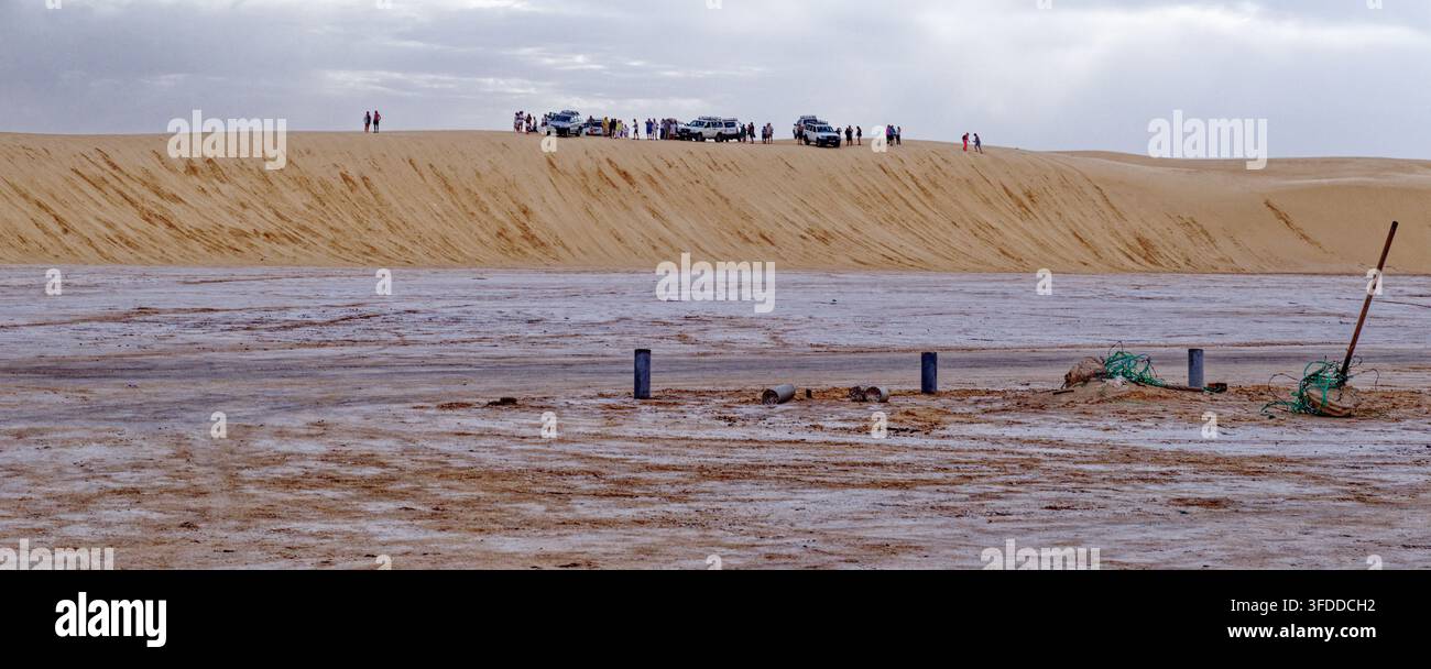 Filea di veicoli fuoristrada 4x4 e turisti parcheggiati sulla cresta di una massiccia duna di sabbia che si affaccia sulle pianure di sale bianche di Hammat-al-Jarid. Catturato Foto Stock