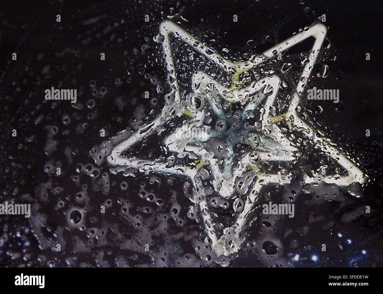 Gocce di pioggia sul vetro contro uno sfondo scuro, con una stella luminosa, con accenti neri e bianchi e un'atmosfera riflessiva e malinconica, oggetti vicini, circondati Foto Stock