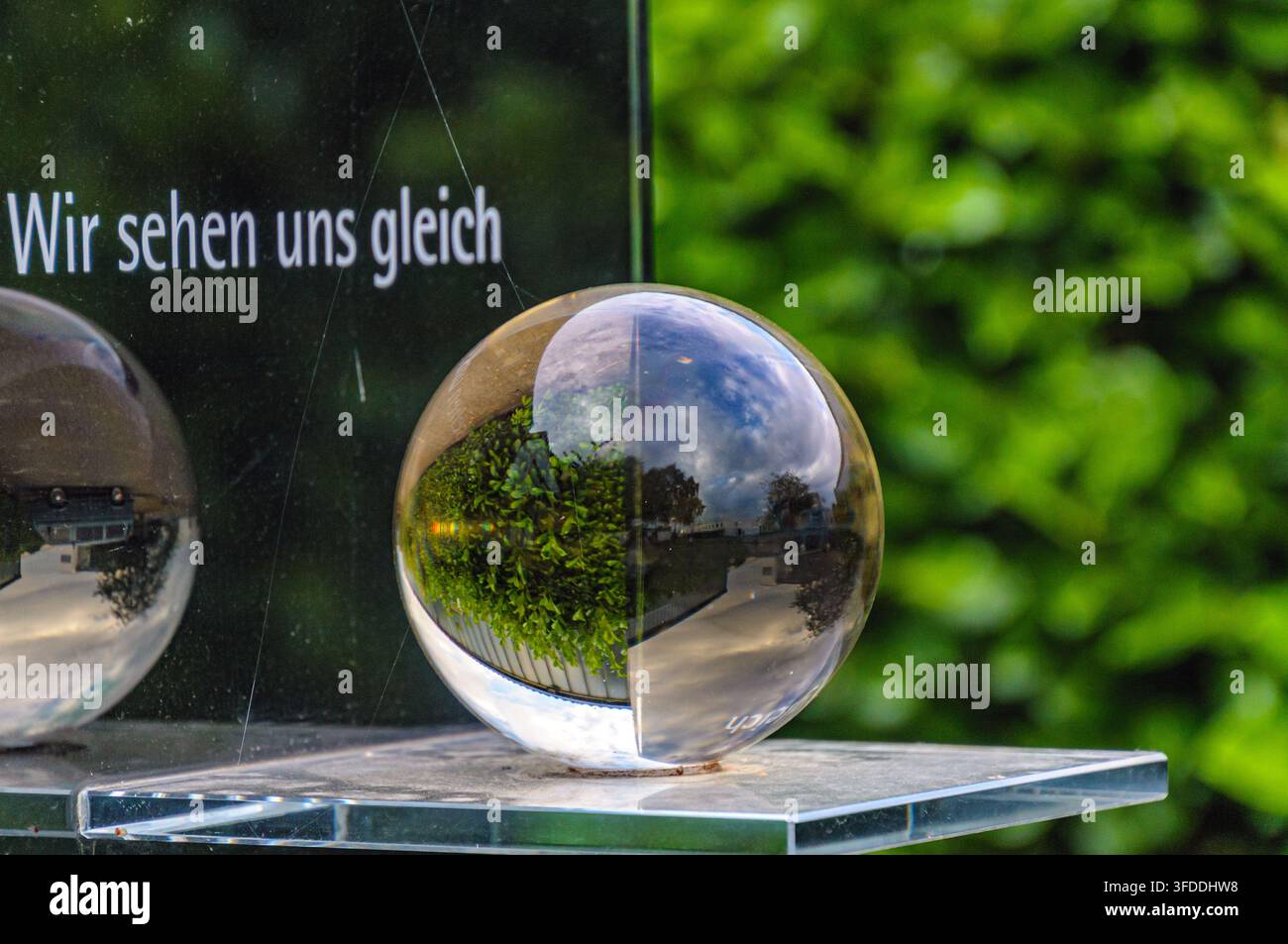 Sfera di vetro che riflette la vegetazione circostante con un cartello che recita "Wir sehen uns gleich" a Coesfeld, Germania Foto Stock