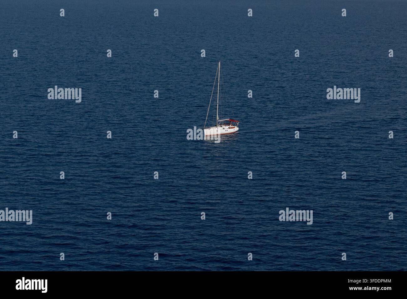 Barca a vela solitaria che galleggia sulle acque calme e blu profondo dell'oceano aperto Foto Stock