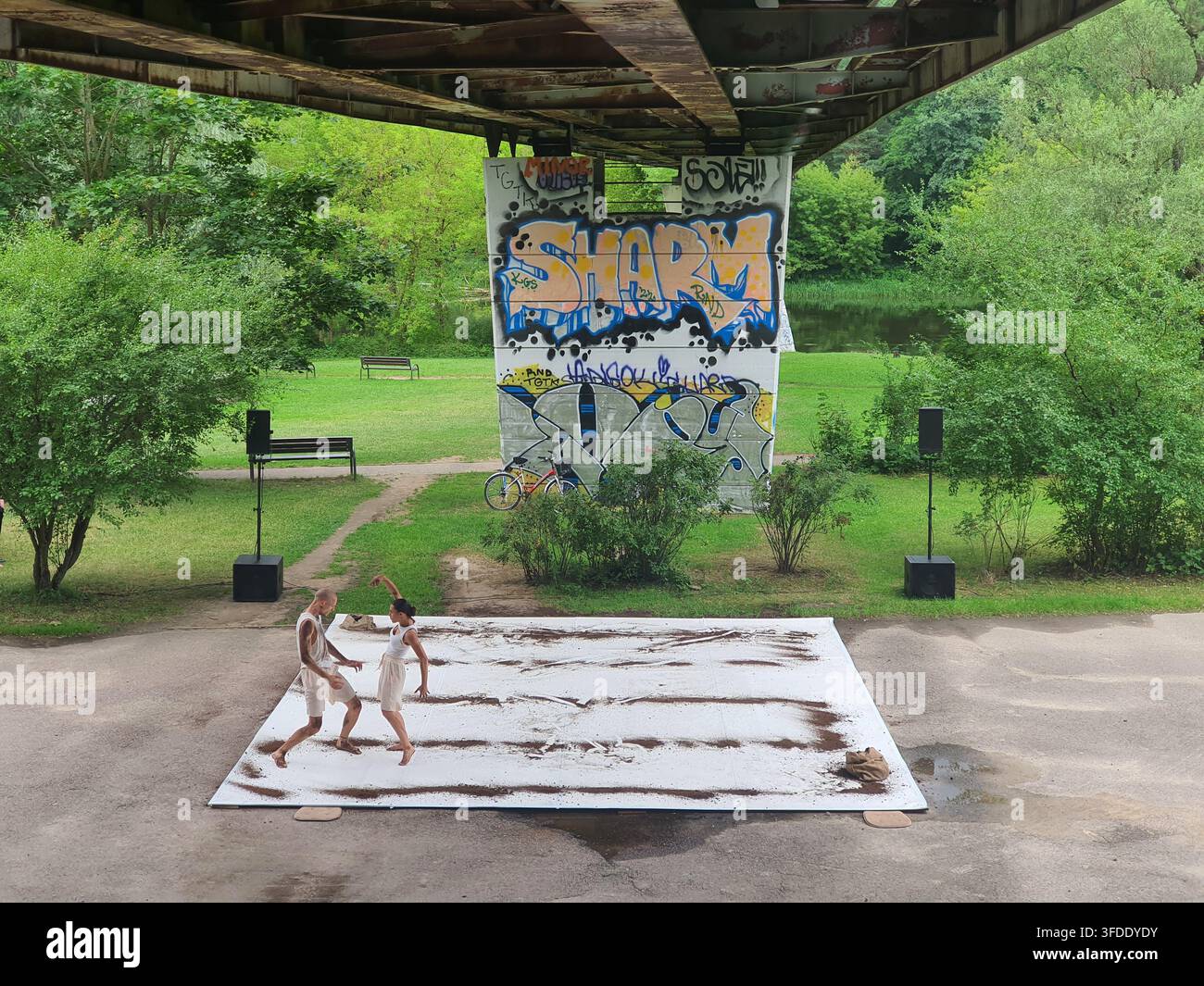 Due ballerini interpretano una danza contemporanea su un grande tappeto bianco posizionato su un terreno di cemento sotto un ponte o una sopraelevata. I ballerini maschi e femmine indossano Foto Stock