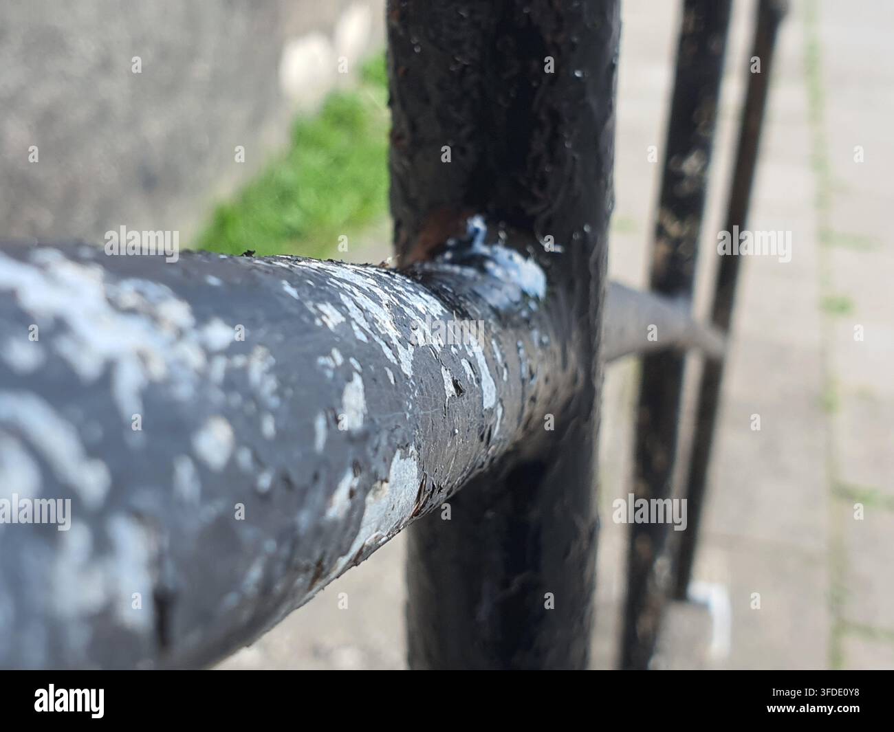 Fotografia ravvicinata di barre di una recinzione in metallo nero consumate con vernice significativamente scrostata e scheggiata a un giunto saldato. Il tubo metallico orizzontale Foto Stock