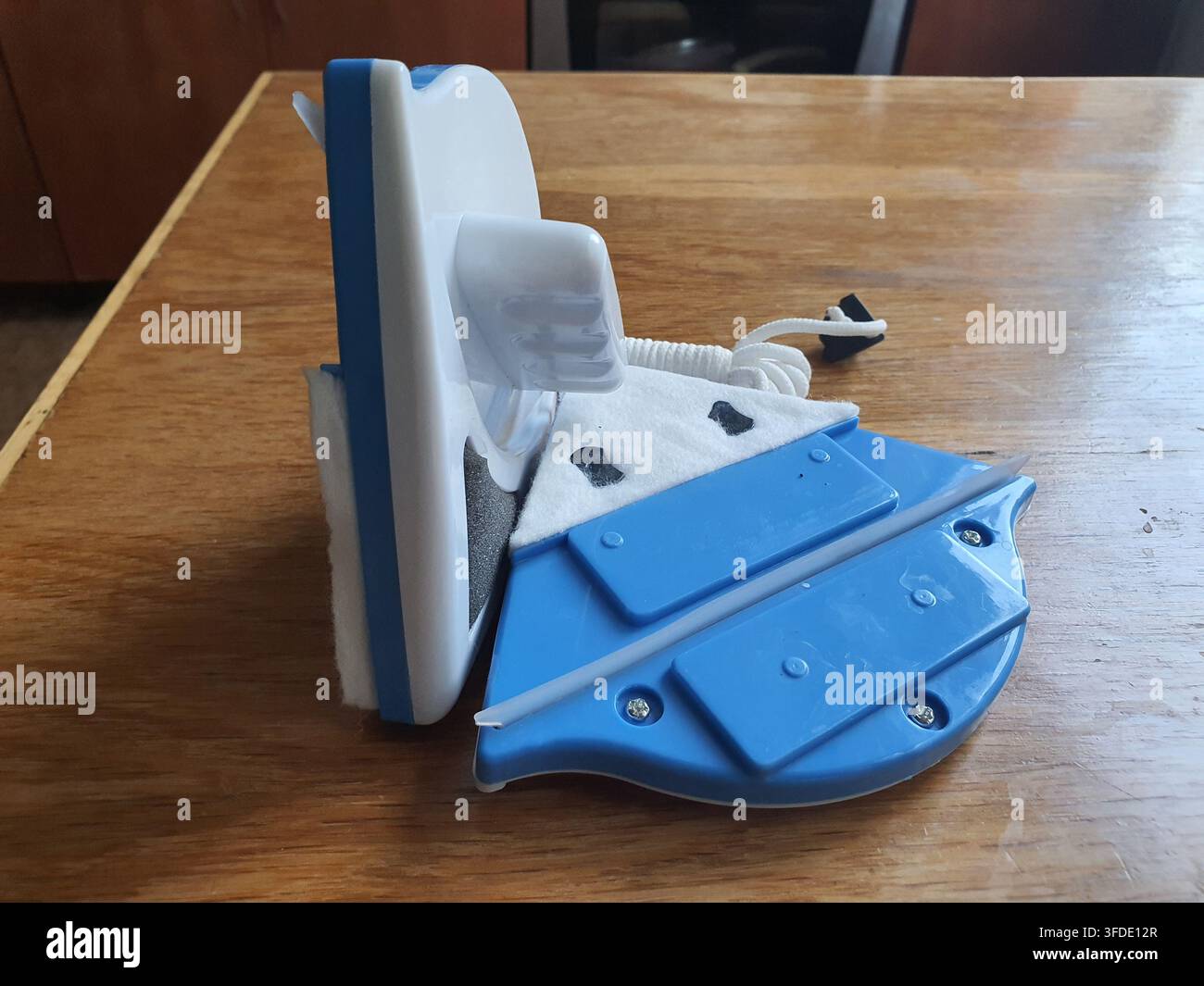 Uno strumento per la pulizia delle finestre magnetico blu e bianco posizionato su una superficie di legno. Il dispositivo è composto da due metà magnetiche separabili - una metà Foto Stock