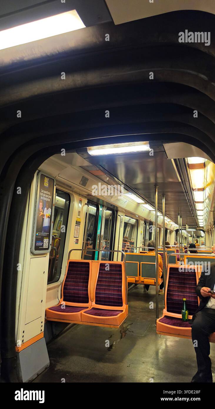 Vista interna di un vagone della metropolitana di Parigi con sedili arancioni e viola, passaggio illuminato e passeggeri seduti in viaggio. Foto Stock