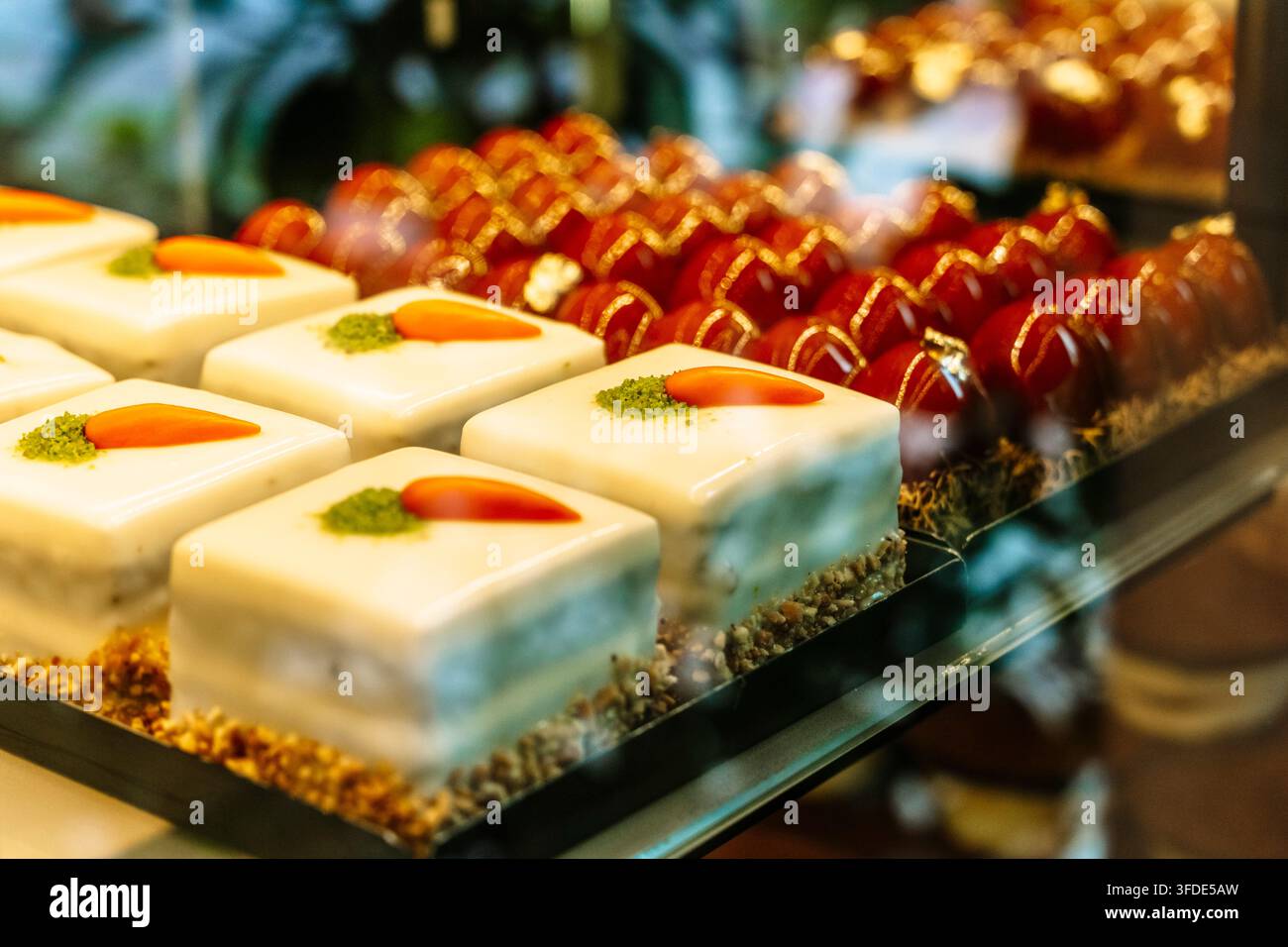 Pasticcini gourmet assortiti con glassa bianca e dolci con specchio rosso in una vetrina di pasticceria. Foto di alta qualità Foto Stock