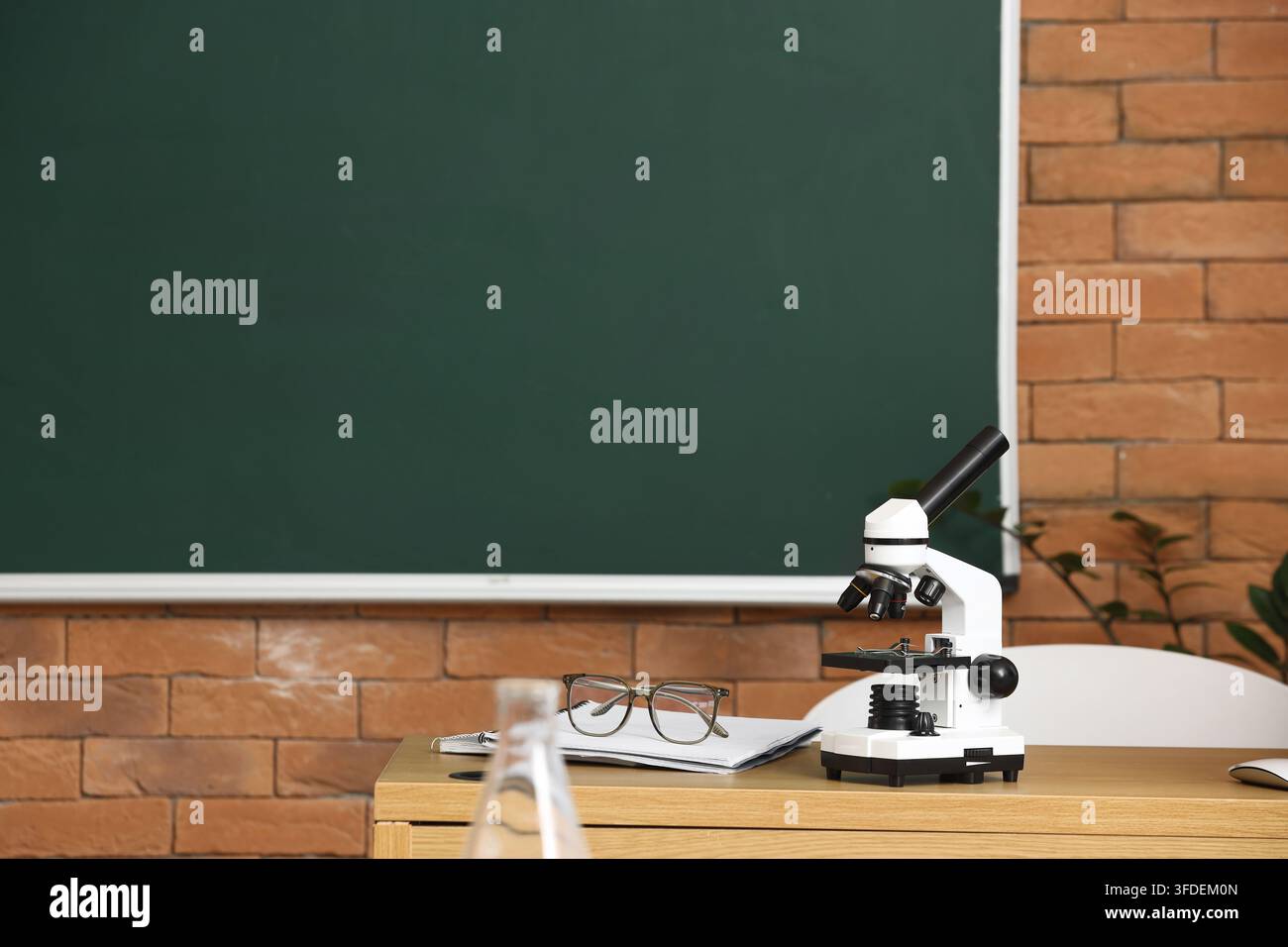 Educazione e ricerca scientifica, microscopio su una scrivania in un'aula con una lavagna verde per lo studio accademico e l'ambiente di apprendimento in laboratorio Foto Stock