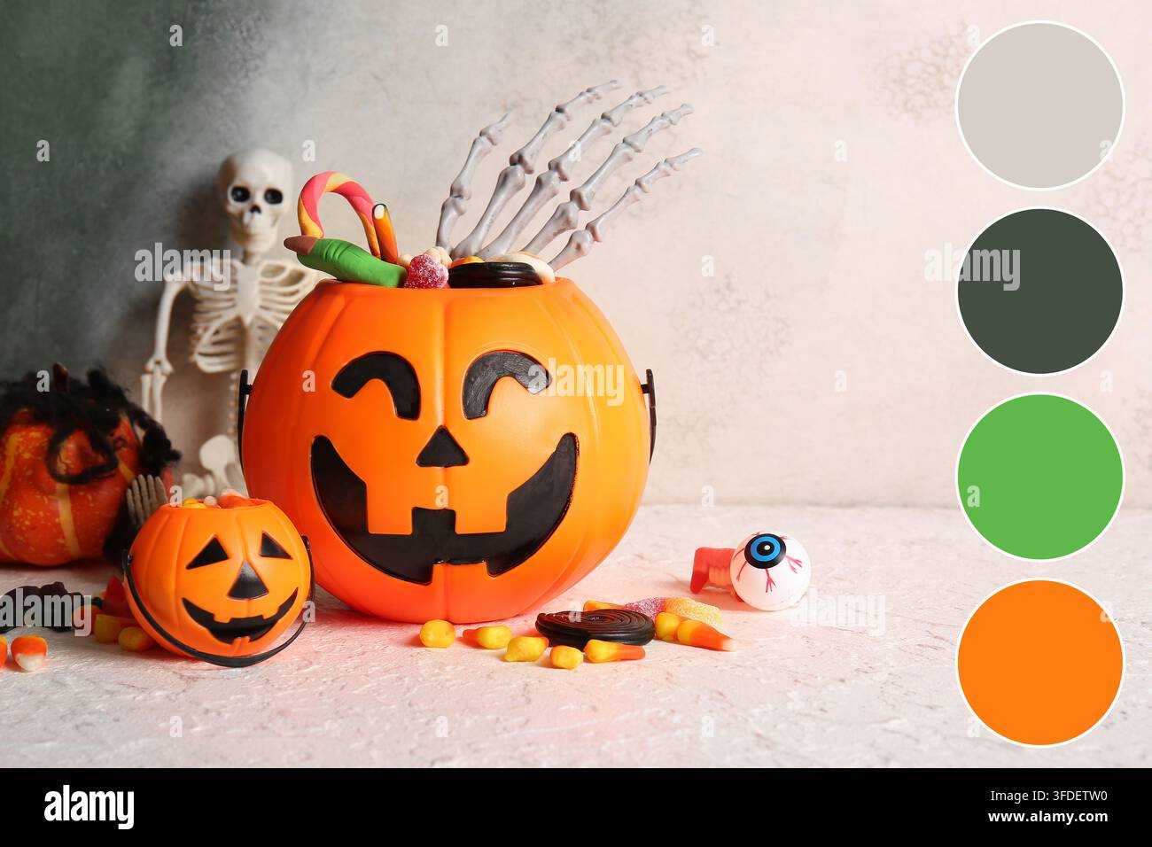 Festa di Halloween e tradizione del dolcetto o scherzetto, secchi di plastica a forma di zucca pieni di caramelle e accessorio mano di scheletro su uno sfondo chiaro texture Foto Stock