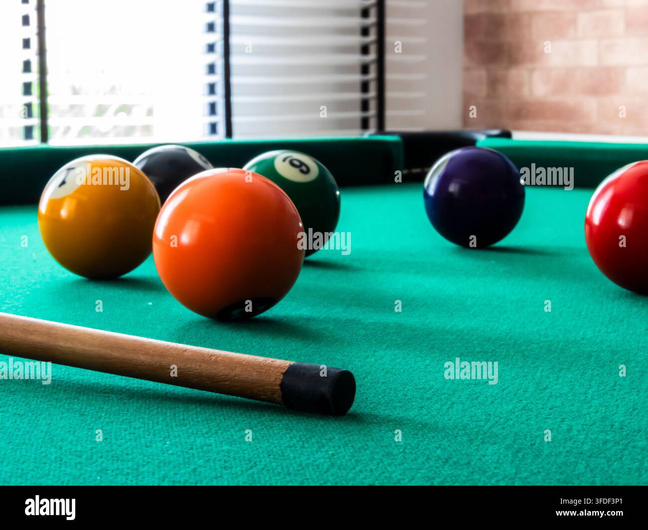 Primo piano di palle da biliardo e stecca su tavolo di feltro verde. Un piano a fuoco selettivo delle palle numerate colorate sparse su un tavolo da snooker verde con Foto Stock