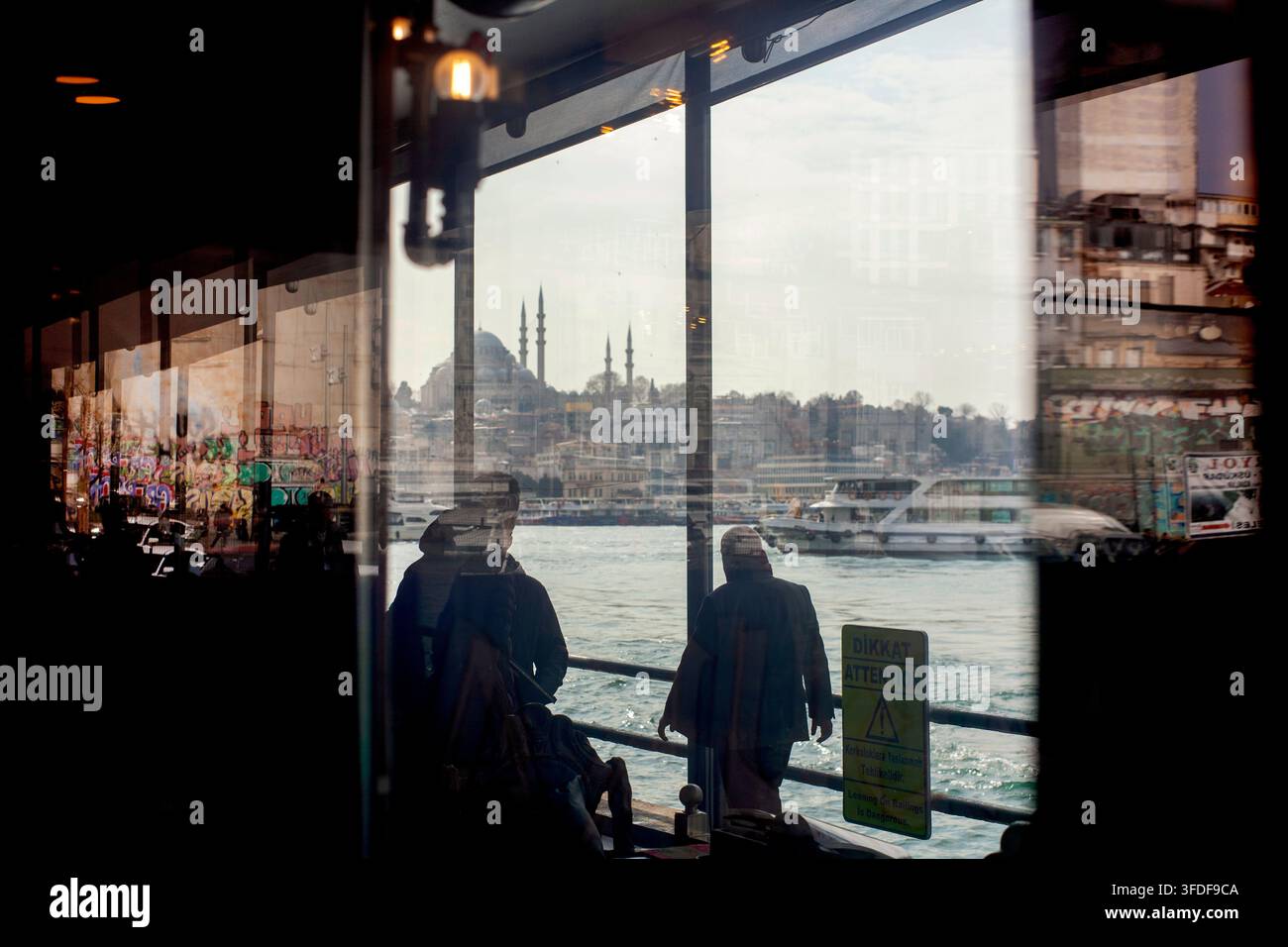 Istanbul, Turchia, 6 marzo 2026. Persone che passeggiano accanto al Corno d'Oro, viste attraverso la finestra di un ristorante sul lungomare. Foto Stock
