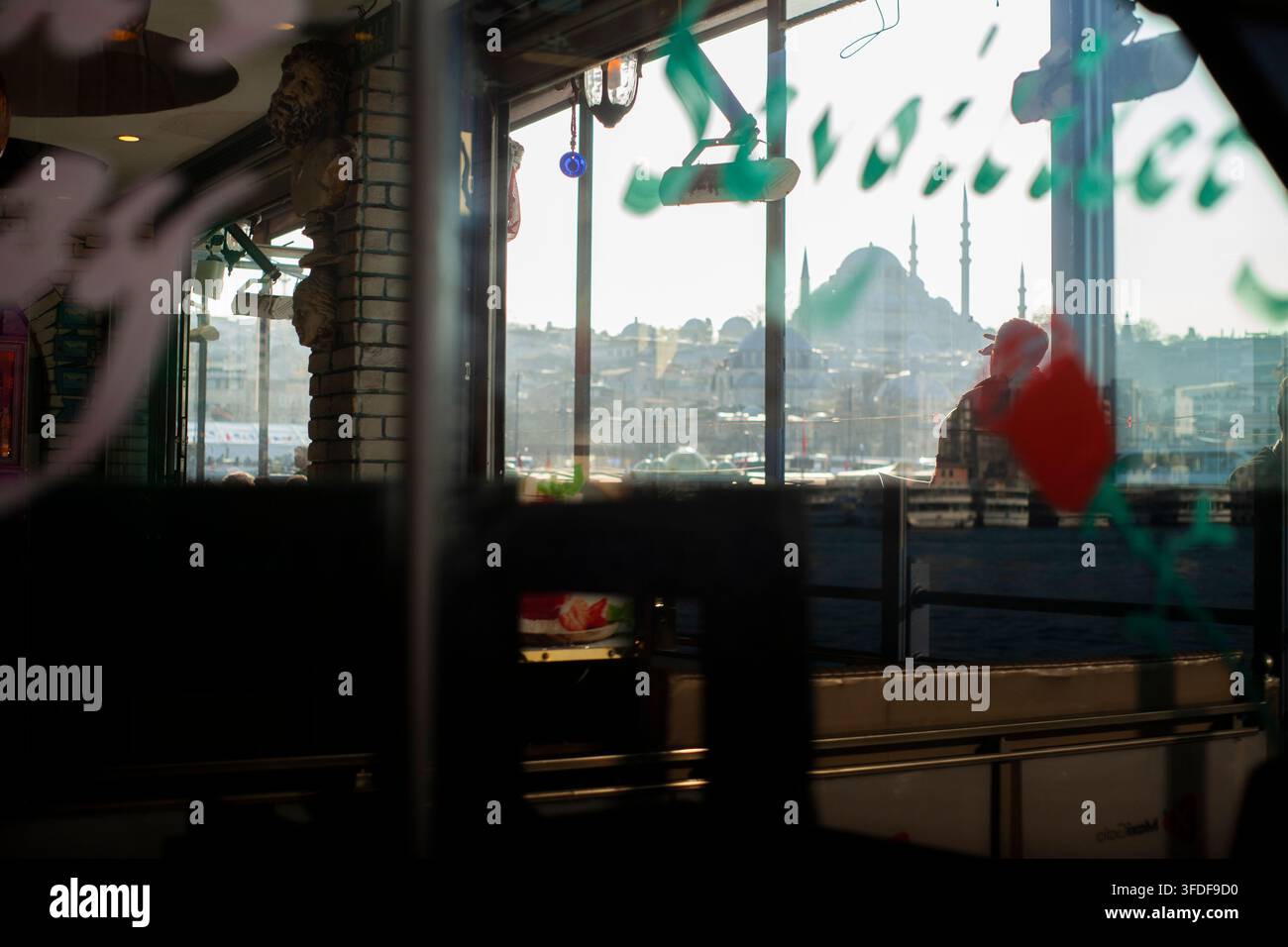 Istanbul, Turchia, 6 marzo 2026. Persone che passeggiano accanto al Corno d'Oro, viste attraverso la finestra di un ristorante sul lungomare. Foto Stock