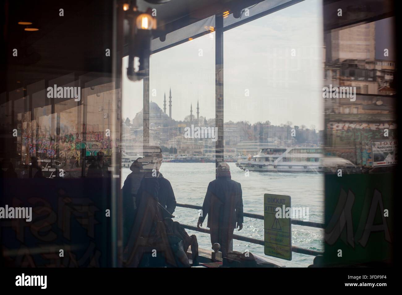 Istanbul, Turchia, 6 marzo 2026. Persone che passeggiano accanto al Corno d'Oro, viste attraverso la finestra di un ristorante sul lungomare. Foto Stock