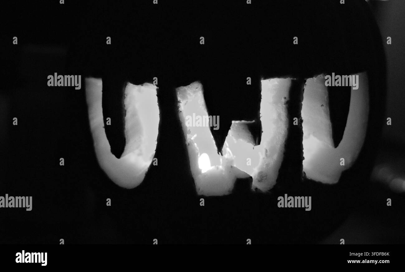 Primo piano di lettere di zucca intagliate che compongono la parola 'UWI', che brillano caldamente nell'oscurità. La luce arancione evidenzia i bordi ruvidi e irregolari di ogni lettera. Ideale per H Foto Stock