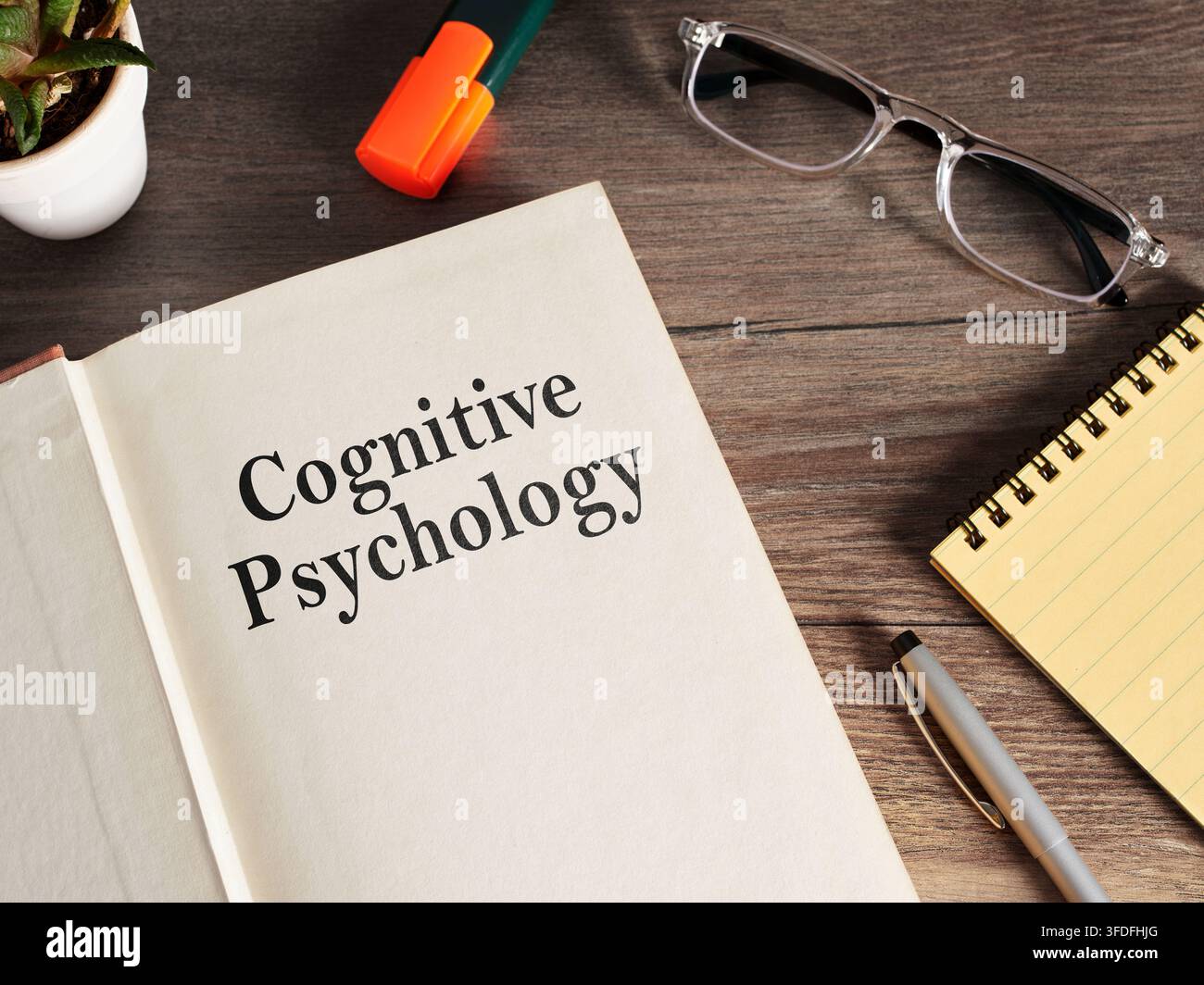 Manuale di psicologia cognitiva su una scrivania di legno, circondato da occhiali, una penna, un blocco note e un evidenziatore per studiare Foto Stock