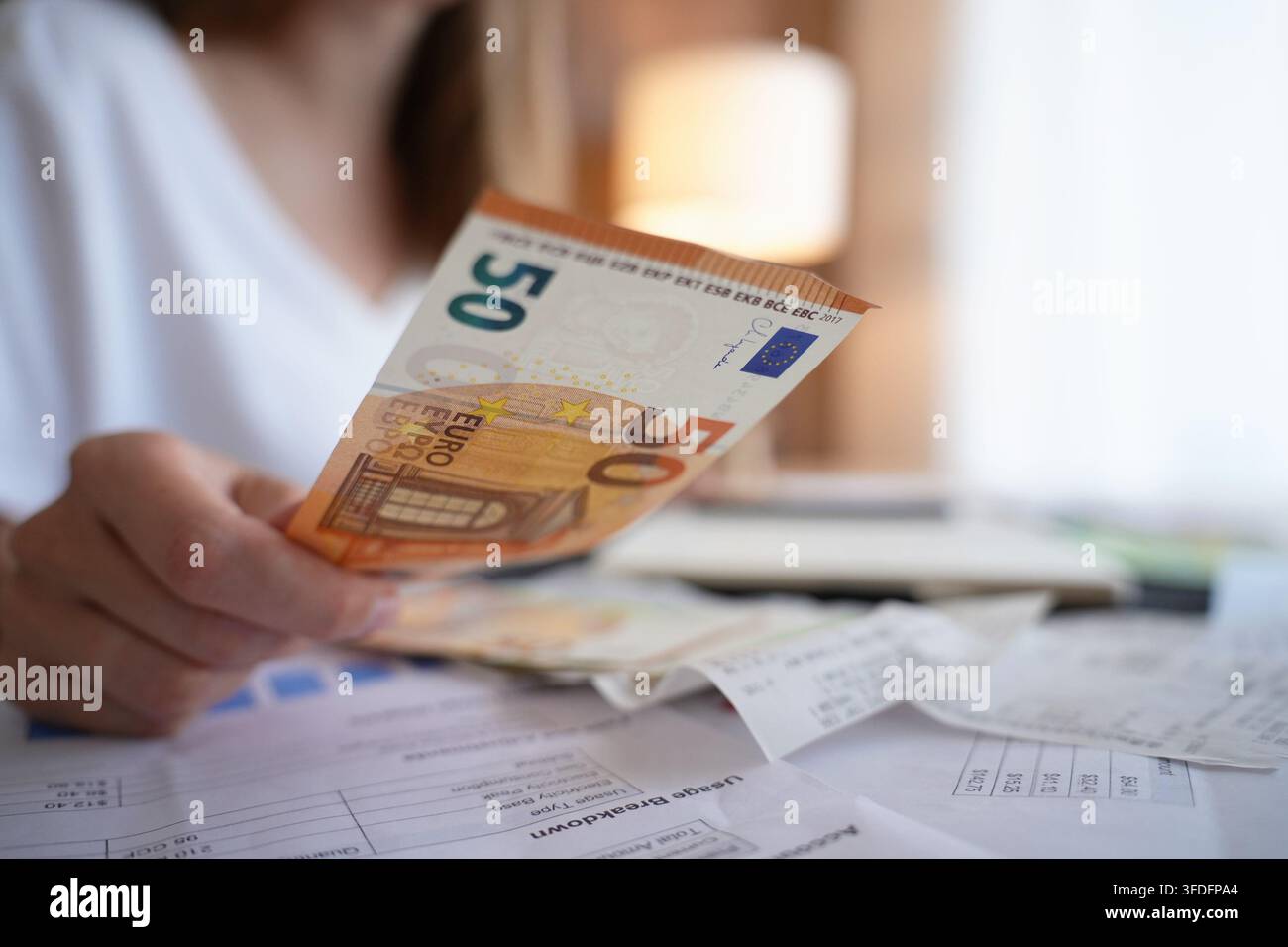 Donna che tiene banconote in euro mentre guarda fatture e ricevute a casa. Finanza personale, budget e gestione delle spese quotidiane. Foto Stock
