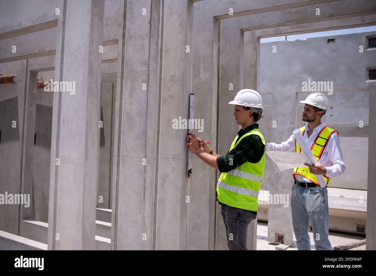 Ingegneri edili che indossano caschi e giubbotti riflettenti stanno lavorando insieme all'interno di una struttura in cemento parzialmente costruita Foto Stock