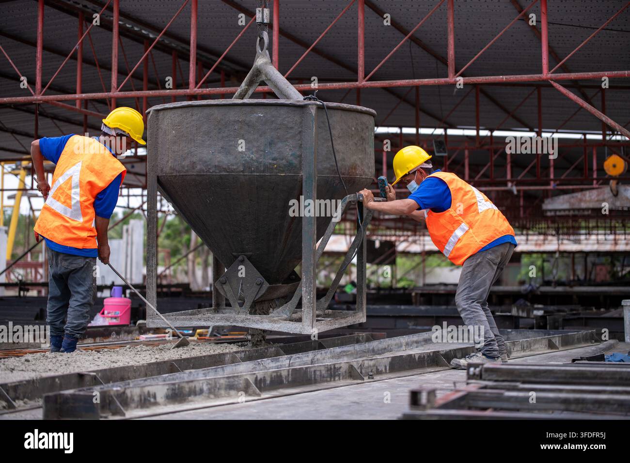 Lavorante edile con casco protettivo, giubbotto di sicurezza e maschera facciale che liscia il cemento bagnato in cantiere Foto Stock