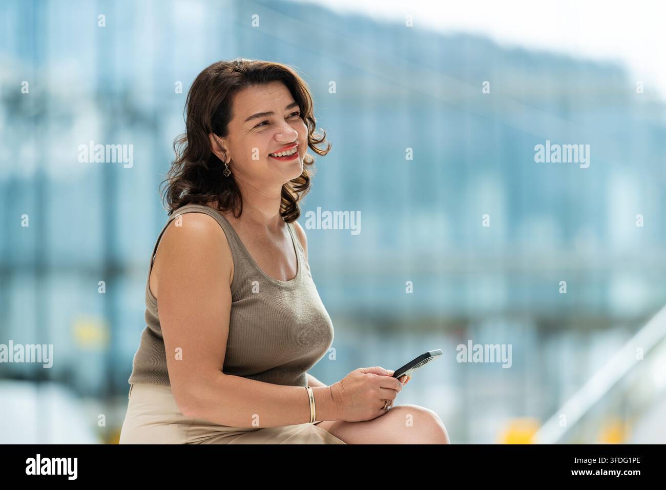 Donna matura sorridente che tiene uno smartphone in città Foto Stock