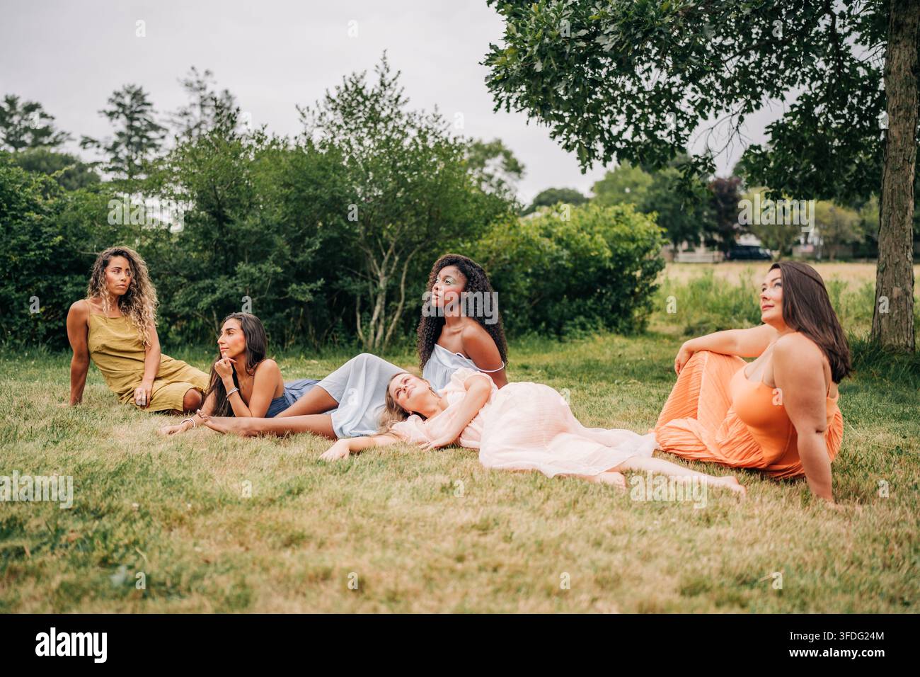 Cinque donne diverse che si rilassano sull'erba all'aperto Foto Stock