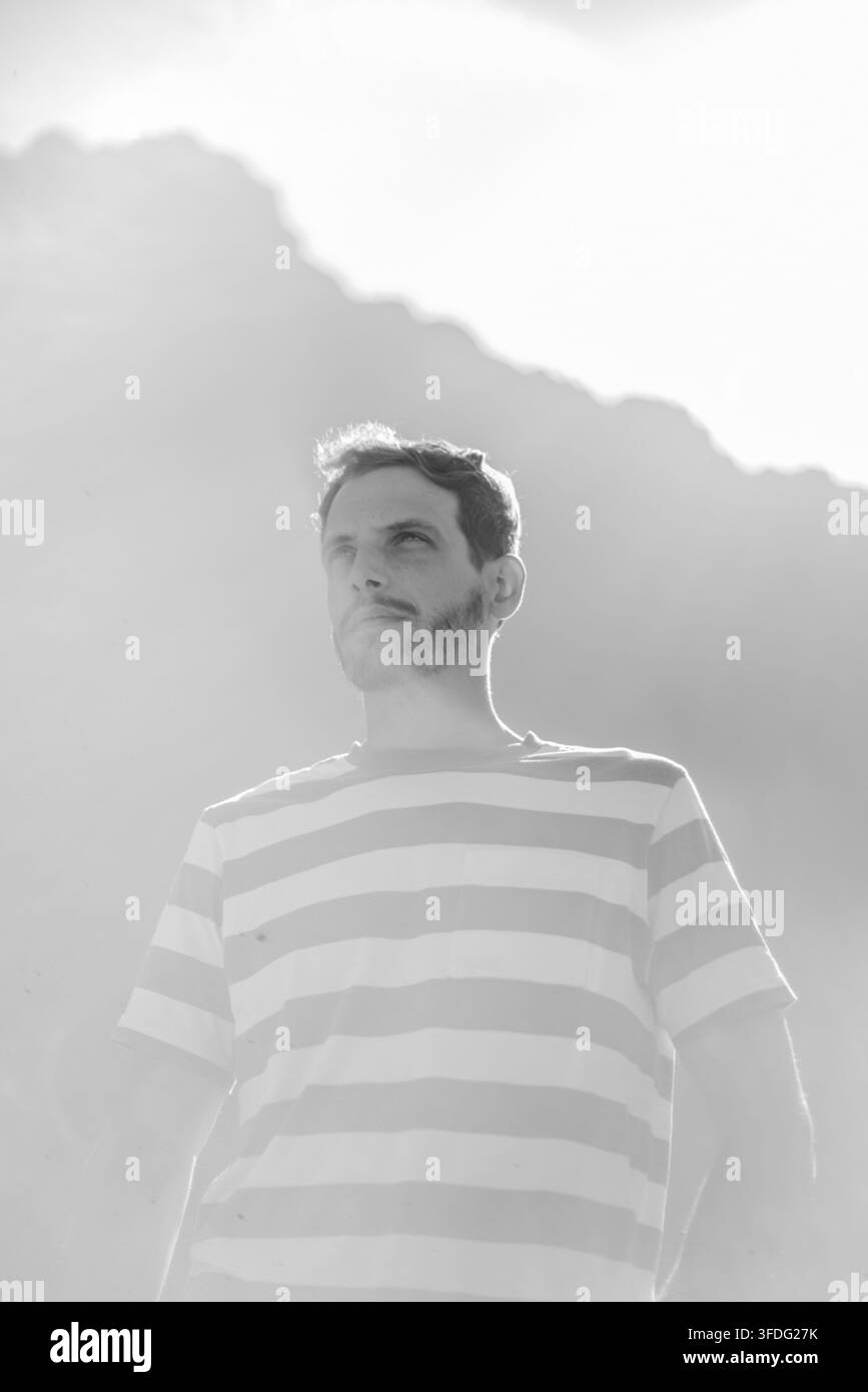 Uomo barbuto in camicia a righe che guarda verso l'alto all'aperto Foto Stock