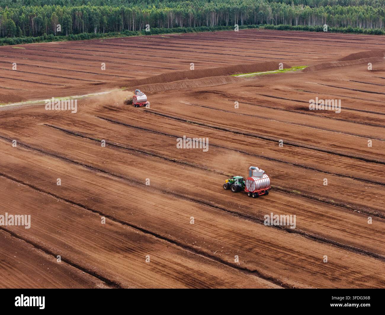 Vista aerea di campi di estrazione della torba industriale con trattori che raccolgono la torba a Laidzes pagasts, Talsu novads, Lettonia. Foto Stock