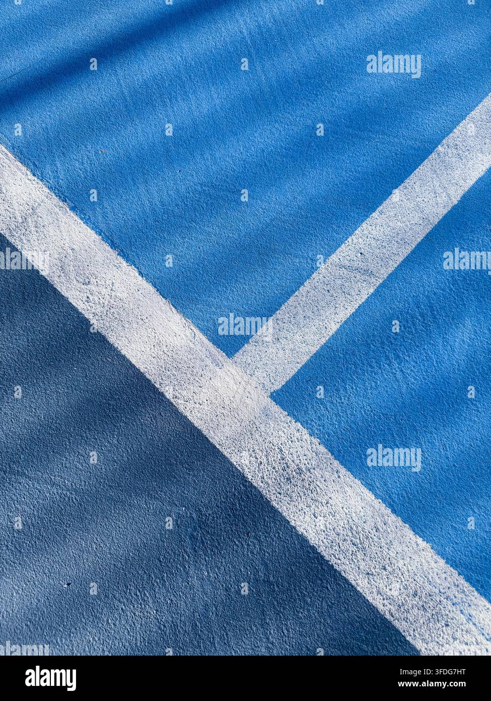 Superficie blu strutturata di un campo da tennis, padel o pickleball con linee bianche intersecanti e ombre che creano contrasto Foto Stock