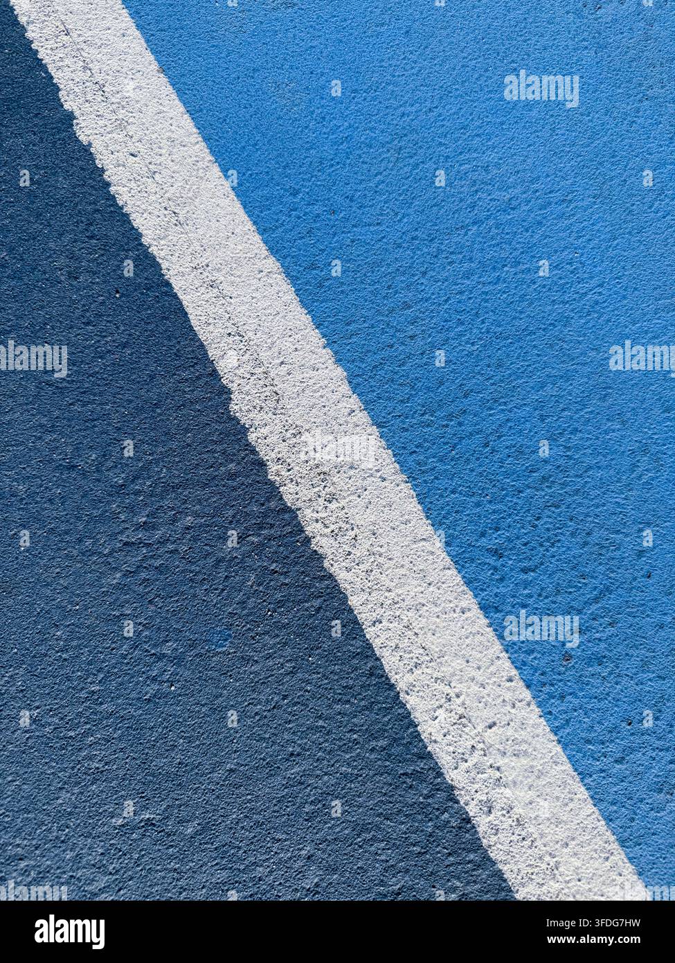 Linea di confine bianca divide una superficie di campo sportivo testurizzata blu chiaro e blu scuro, motivo geometrico astratto in primo piano e contrasto di colori Foto Stock