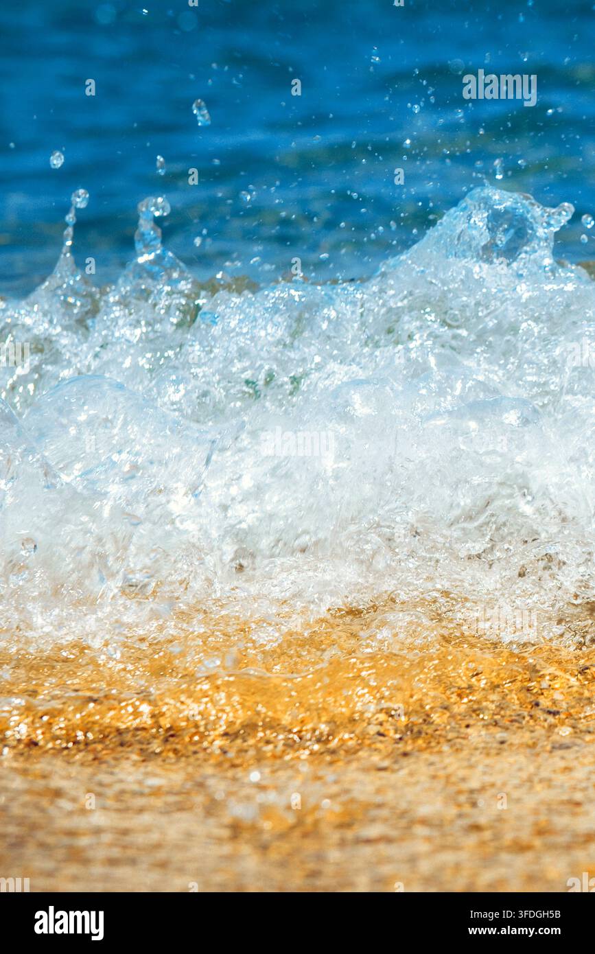 Vista ravvicinata di un'onda del mare che rotola dolcemente su una spiaggia di sabbia, con l'acqua schiumosa dell'oceano che si sparge lungo la linea costiera. Scena costiera naturale con Foto Stock
