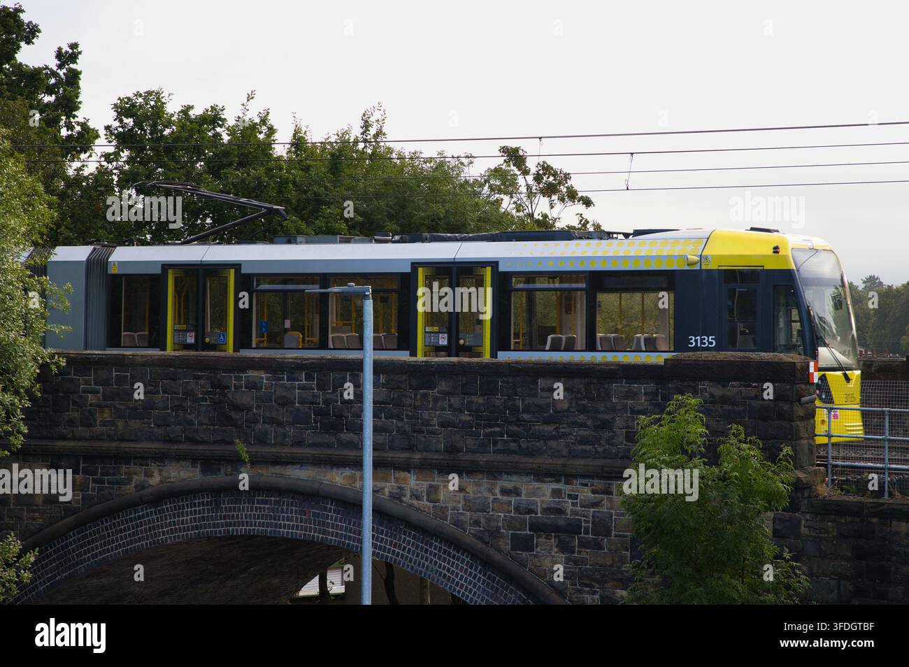 Moderna tramvia leggera attraversa il ponte di pietra storico sopra Spring Lane a Radcliffe, Lancashire, Regno Unito. Foto Stock