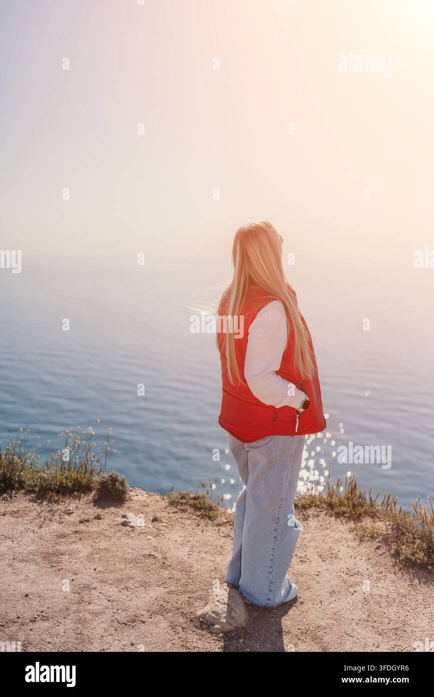 Donna vista di spalle con vista sull'oceano da una scogliera rocciosa, che guarda il mare con spazio libero Foto Stock