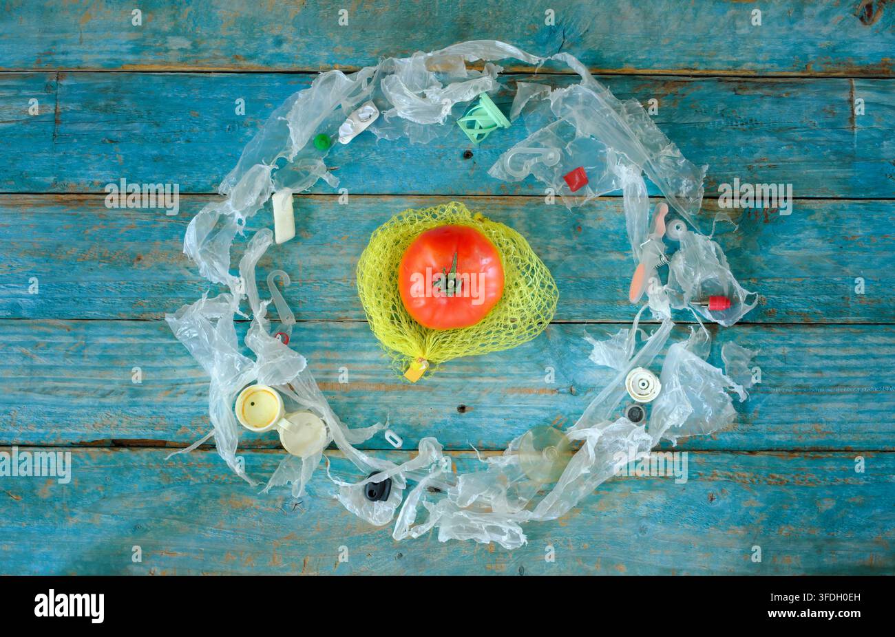Inquinamento di verdure e altri alimenti con microplastica, Inquinamento di verdure e altri alimenti con microplastica, un singolo pomodoro circondato da plastica Foto Stock