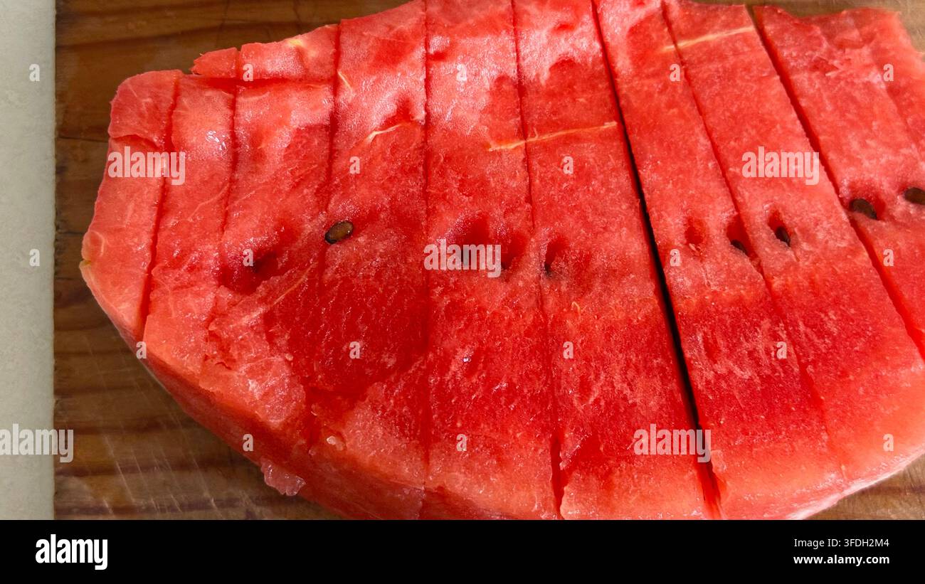 Anguria fresca tagliata in più fette su un tagliere di legno, che illustra la frutta estiva, la preparazione del cibo e gli spuntini salutari. Foto Stock