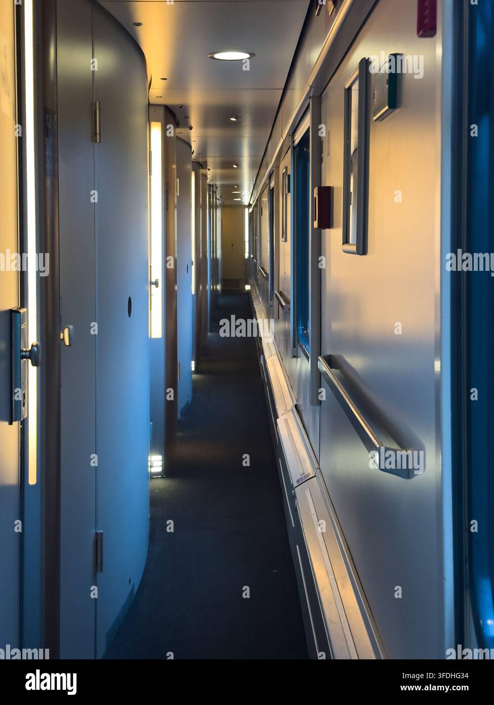 Un corridoio del treno passeggeri si estende attraverso scompartimenti collegati con illuminazione moderna. La scena rappresenta viaggio, movimento e connessione. Foto Stock