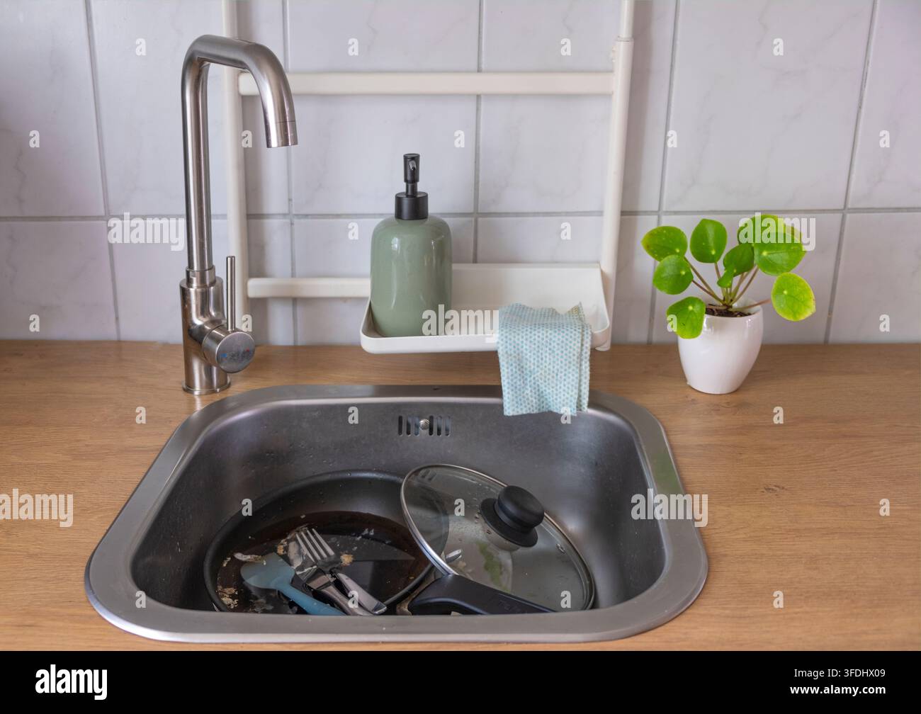 Piatto e padella sporchi posizionati in un lavandino da cucina con schiuma di sapone, che rappresentano il lavaggio quotidiano della vaissella e le faccende domestiche. Foto Stock