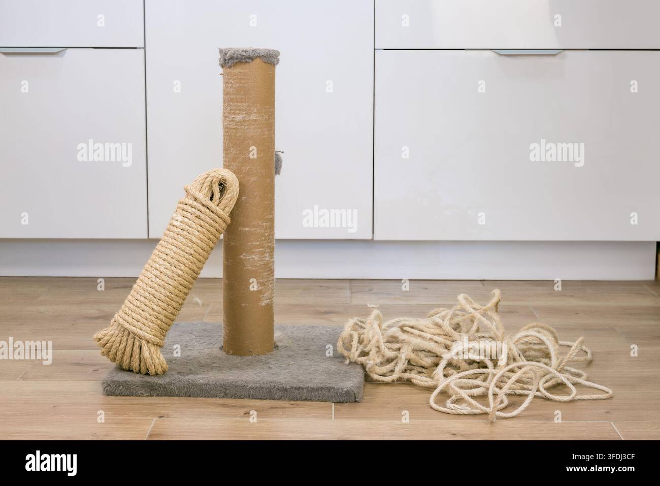 Albero per gatti con corda di sisal di ricambio, colonna di cartone e fibre sciolte su una base grigia in una stanza con armadio bianco Foto Stock