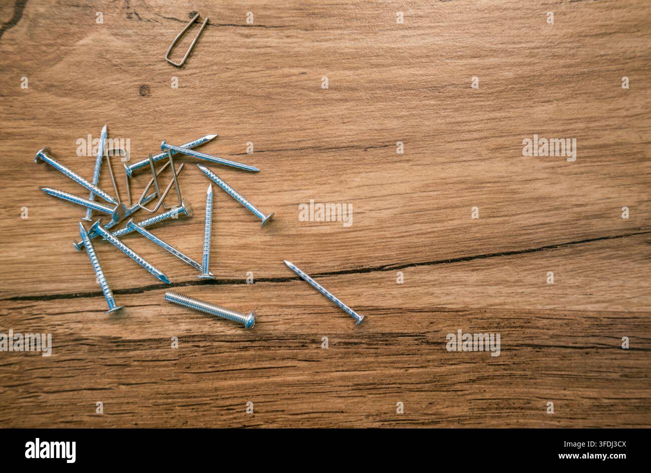 Chiodi argentati sparsi e fissaggi metallici su un tavolo di legno stagionato, che mostra venature, nodi, crepe e un'ampia area vuota Foto Stock