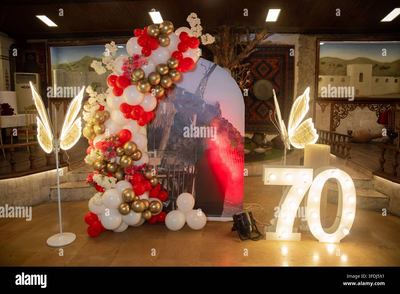 Il numero 70 illuminato della tenda aggiunge un tocco elegante allo sfondo della festa di anniversario. Allestimento di stand estivo per una celebrazione del 70° compleanno decorata Foto Stock