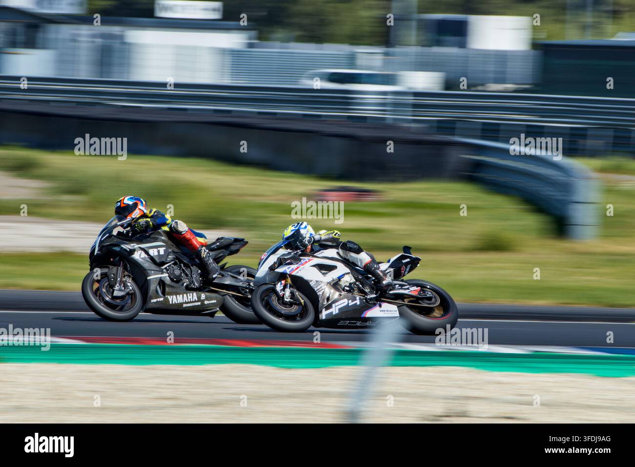 Scatto d'azione dinamico di due piloti di moto sportive che si piegano stretti in una curva, gareggiando testa a testa per la posizione su una pista di corsa asfaltata soleggiata. Foto Stock