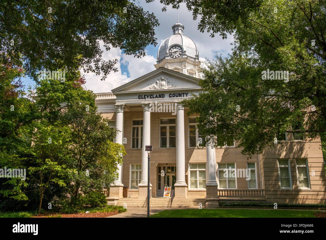Il tribunale storico della contea di Cleveland a Shelby, Carolina del Nord, presenta una torre dell'orologio a cupola e colonne corinzie bianche, incorniciate da una vegetazione verdeggiante Foto Stock