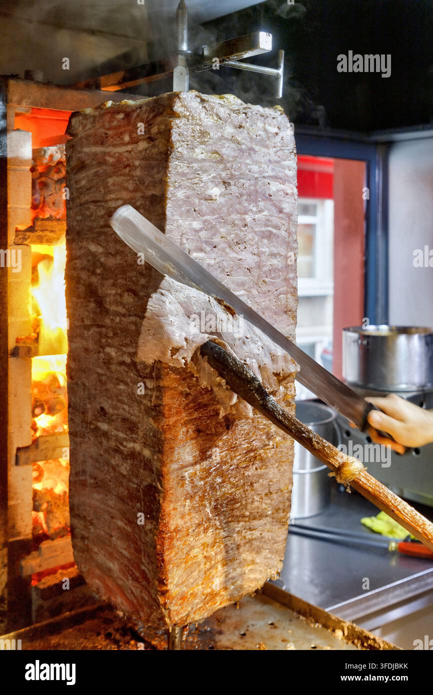Chef cuoco che taglia sottili fette di doner kebab di manzo premium Foto Stock