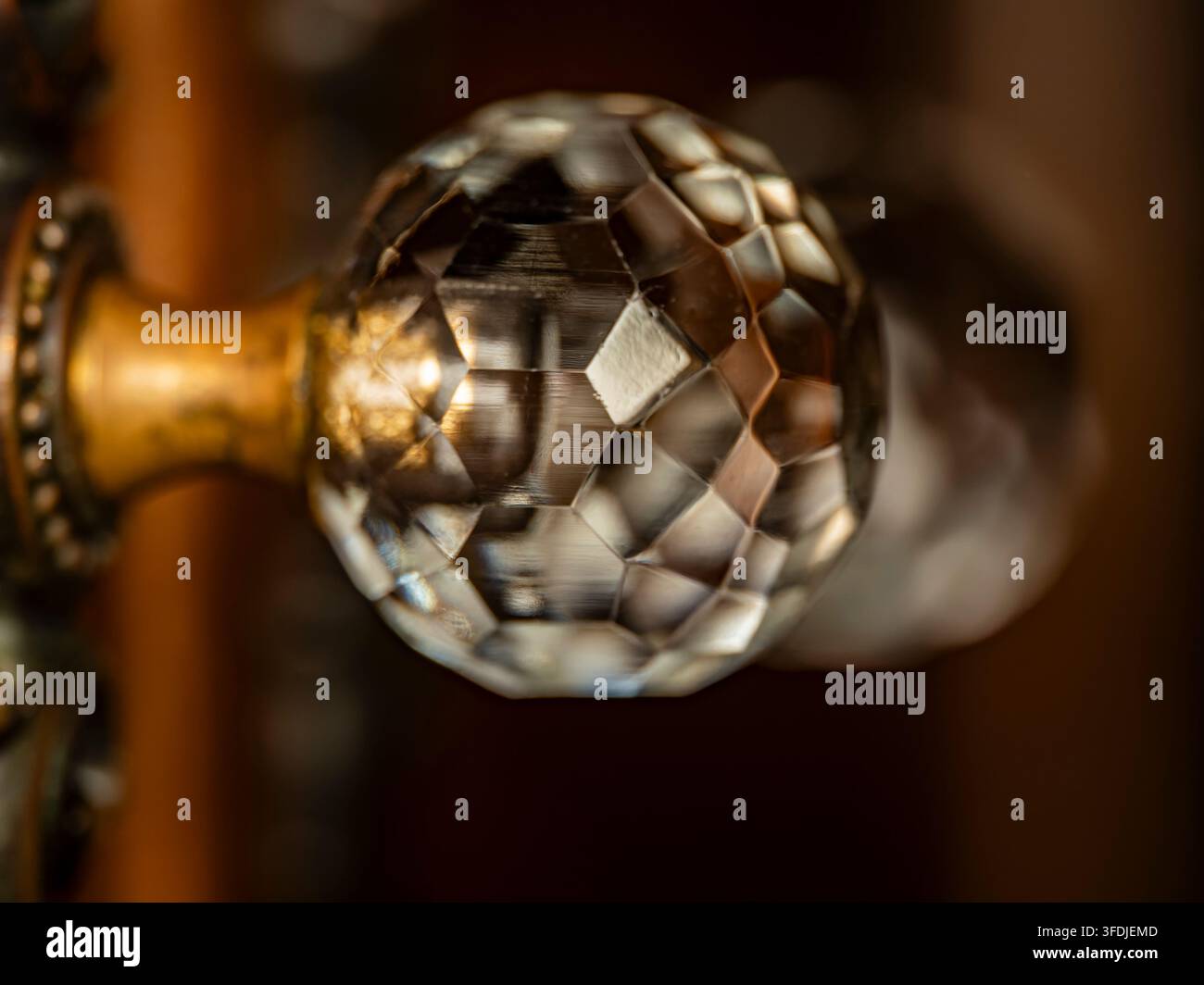 Un primo piano di una maniglia di porta in vetro sfaccettato ornata con ferramenta in ottone che mostra riflessi e bokeh Foto Stock