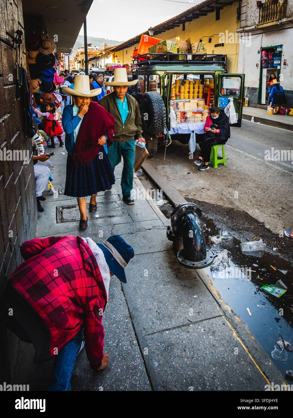 Cajamarca, Perù - 05 novembre 2022: Vista di persone che indossano cappelli tradizionali che camminano lungo una strada, con un veicolo parcheggiato che vende merci sullo sfondo Foto Stock